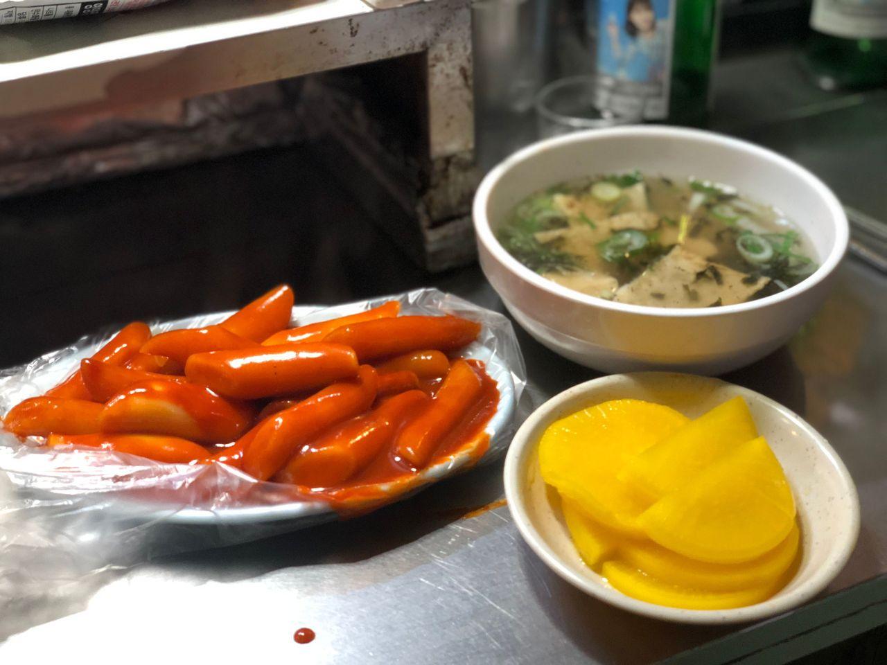 韓國布帳馬車的辣炒年糕伴隨著魚板湯和醃蘿蔔，呈現出一個經典的韓國街頭小吃組合，充滿韓國文化的美食體驗。